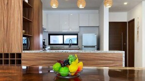 A modern kitchen with a marble countertop, wooden cabinetry, and a fruit bowl. - 4BR House · Sleeps 12 · Shared Pool · Playa (Playa del Carmen)