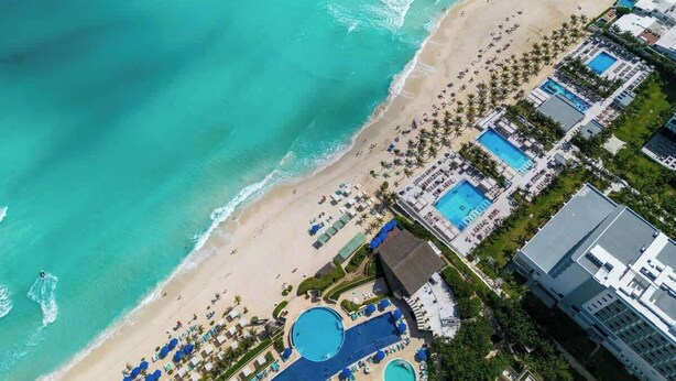 An aerial view of a beach resort with multiple swimming pools, a sandy beach, and a hotel structure. - 2BR Cancun Hotel Zone: Pool, Walk to the Beach (Cancún)