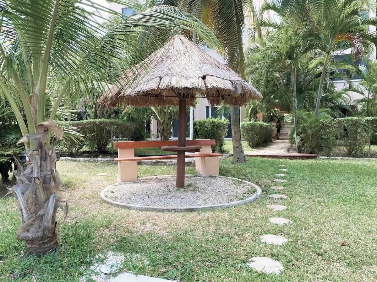 A circular seating area with a thatched roof, surrounded by a gravel path and palm trees.