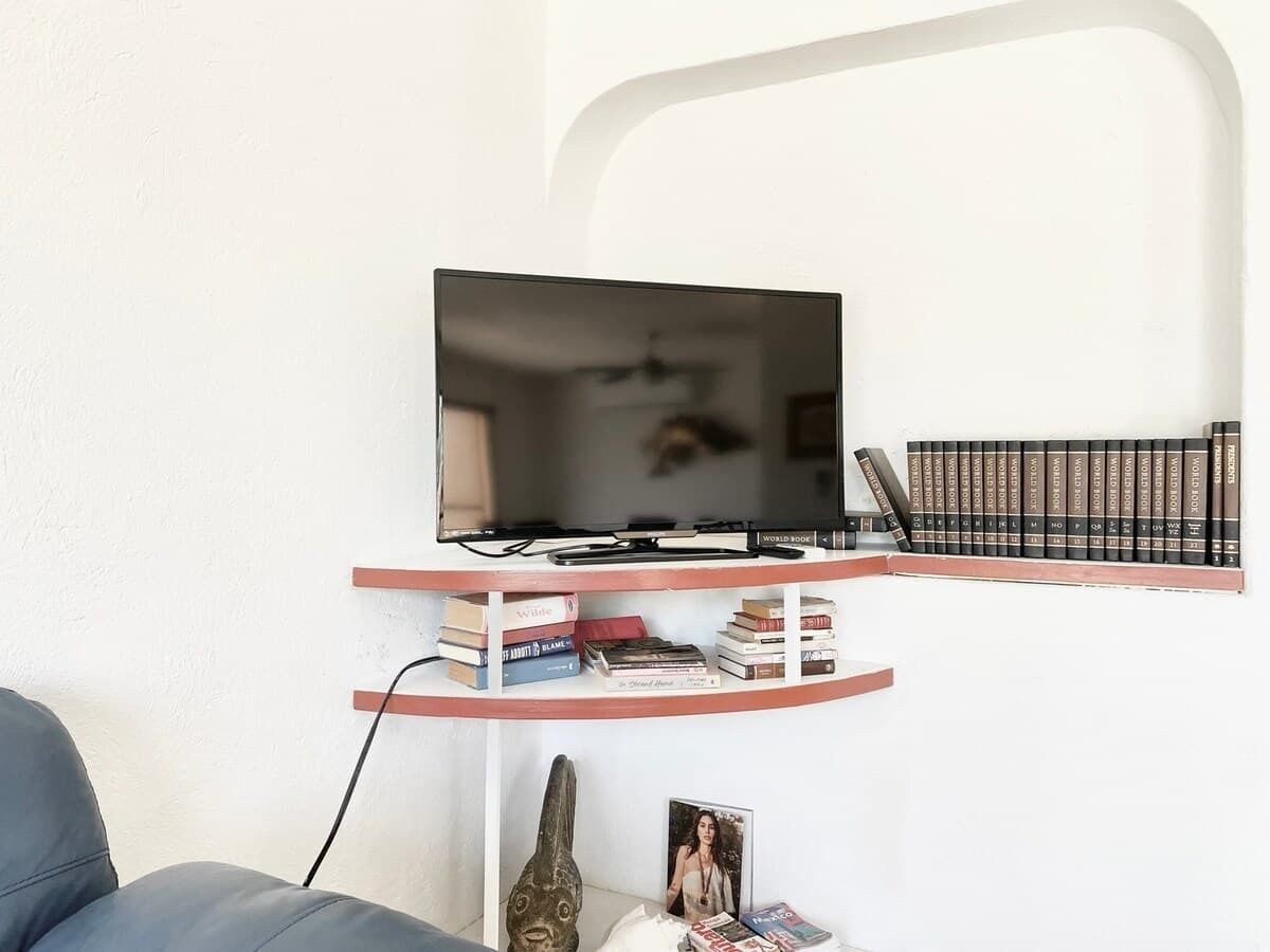 A flat-screen TV on a white wall, a bookshelf with books and a picture frame, and a grey sofa.