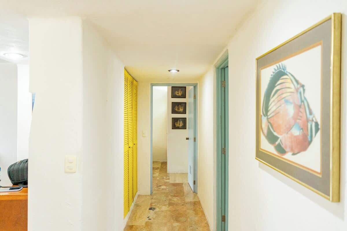 Un couloir doté d’un sol carrelé, d’un tableau encadré accroché au mur et d’une porte dont le cadre est bleu.