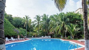 A swimming pool surrounded by palm trees and white lounge chairs. - 2BR Cancun Hotel Zone: Pool, Walk to the Beach (Cancún)