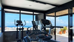 Et fitnesscenter med løbebånd og crosstrainere, store vinduer og udsigt over byen.