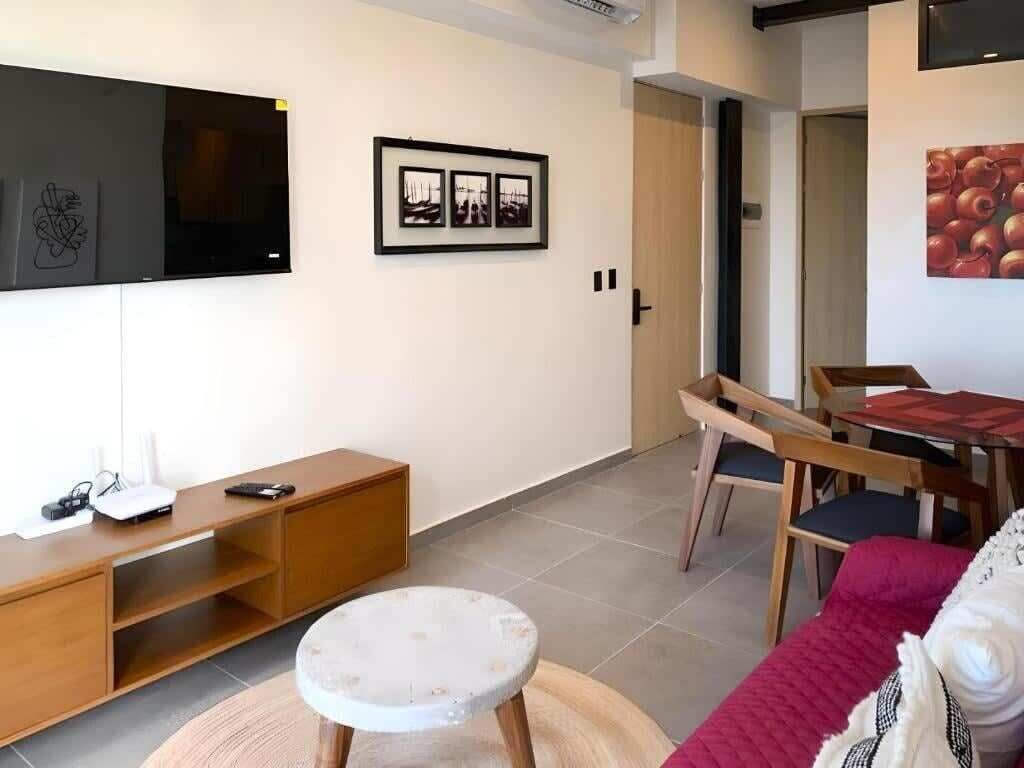Un salon moderne avec un téléviseur à écran plat, un meuble de rangement en bois, une table ronde blanche et un canapé rouge.