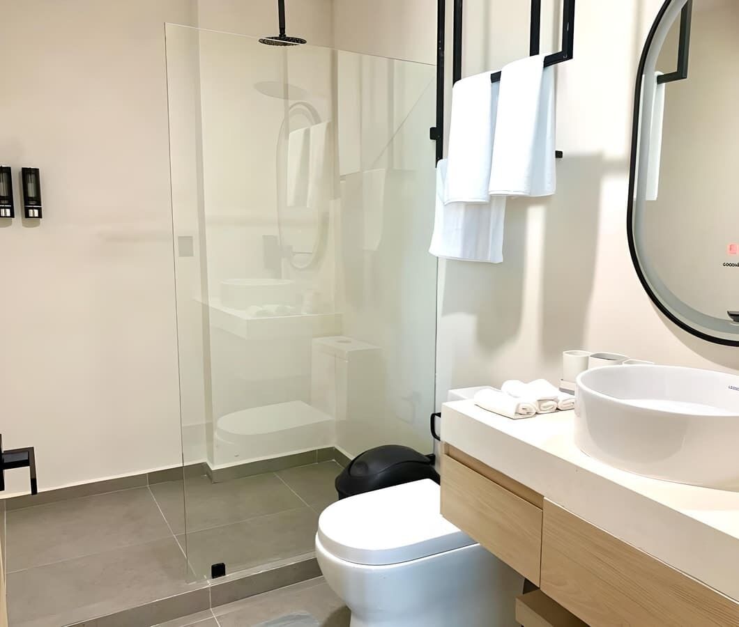 Ein modernes Badezimmer mit Duschkabine aus Glas, einer weißen Toilette, einem Waschbecken mit großer Schüssel und einem Spiegel mit schwarzem Rahmen.