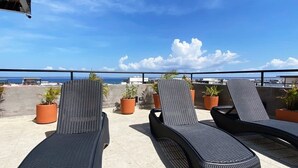 En tagterrasse med liggestole og plantekasser, med udsigt over et vandareal.