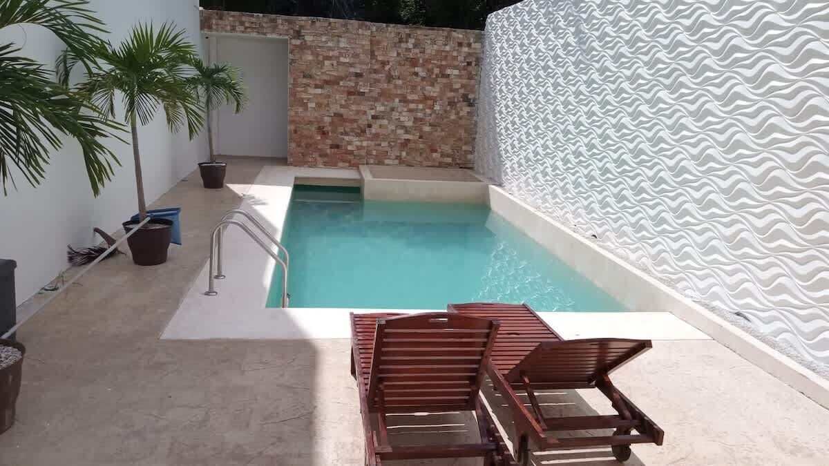 Ein Schwimmbad mit Fliesen umrandet, einer Ziegelwand und einer weißen, strukturierten Wand.