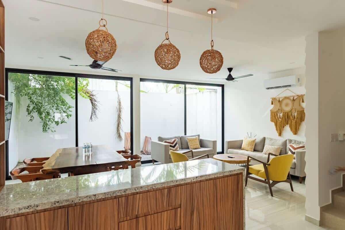 A modern kitchen with a wooden island, large windows, and hanging woven light fixtures.