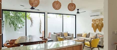 A modern kitchen with a wooden island, large windows, and hanging woven light fixtures.