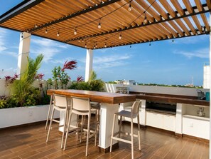 Une cuisine extérieure avec une table et des chaises en bois, un barbecue et une vue sur la ville.
