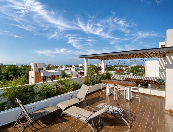 A rooftop terrace with lounge chairs, a table, and a pergola.