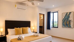 A hotel room with a bed, bedside lamps, an air conditioning unit, a ceiling fan, a window with curtains, and a painting on the wall. - 2BR Apt + Rooftop Pool | Steps to 5th Avenue (Playa del Carmen)