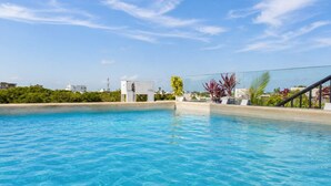 A swimming pool with clear blue water, surrounded by greenery and a clear sky. - 2BR Apt + Rooftop Pool | Steps to 5th Avenue (Playa del Carmen)