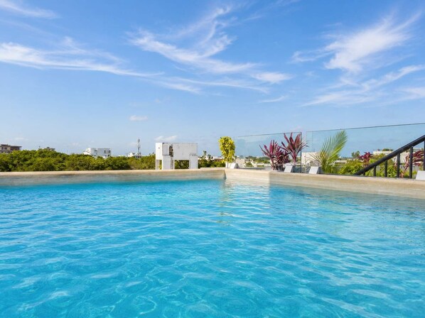 Une piscine d’un bleu éclatant, séparée du reste par une barrière de verre, entourée de verdure et surplombée d’un ciel dégagé.