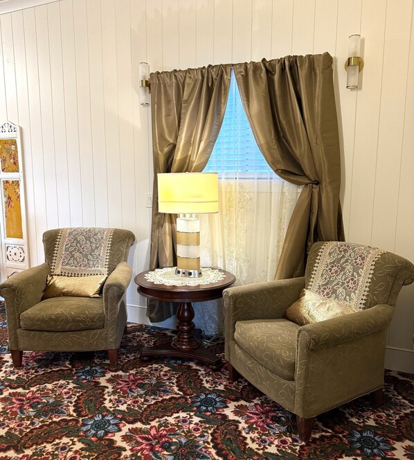 A room with two armchairs, a small table with a lamp, and a patterned carpet. - Whimsy Station (Chugiak)