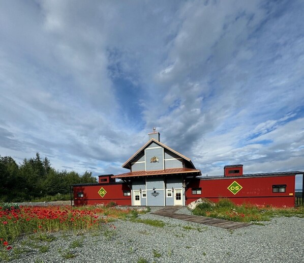 A two-story building with a red and blue facade, a central chimney, and a small garden area with red flowers.