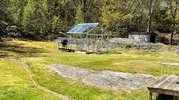 Un espace extérieur verdoyant, avec une structure métallique, peut-être une serre, et un petit abri de jardin.