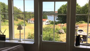 Una habitación con un ventanal grande que da a un área verde con casas y una masa de agua.