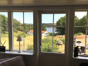 A room with a large window overlooking a grassy area with houses and a body of water.