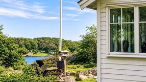 Una casa con un amplio ventanal, un asta de bandera y vistas a un lago y colinas.