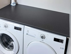 Vue de face d’un appareil combiné comprenant un lave-linge et un sèche-linge, avec leurs panneaux de commande et un écran numérique.