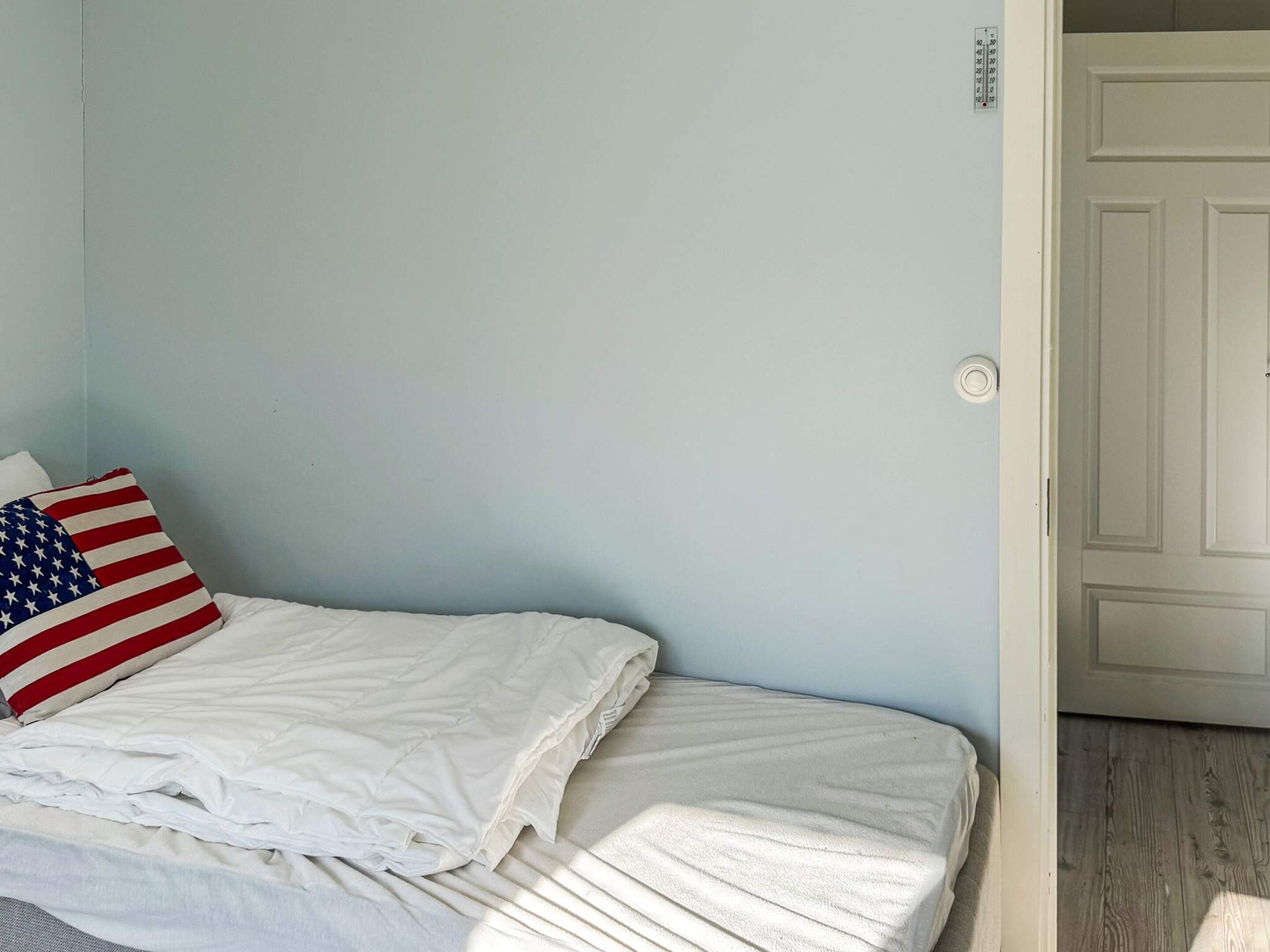 Un lit avec une literie blanche et un oreiller orné du motif du drapeau américain.