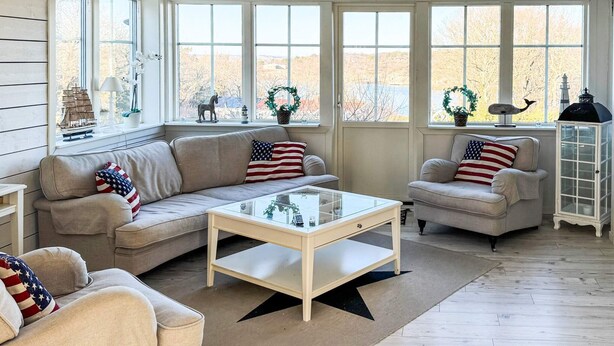 Una sala de estar acogedora con un sofá, sillones y una mesa de centro. Amplios ventanales ofrecen vistas al exterior.