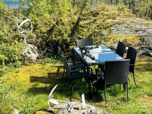 An outdoor dining area with a table and chairs, surrounded by greenery and a rocky landscape. - 5 Star Holiday Home in Marstrand (Marstrand)