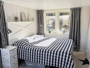 Une chambre à coucher comprenant un lit, une lampe de chevet, une fenêtre avec des rideaux et une étagère murale agrémentée d’objets décoratifs.