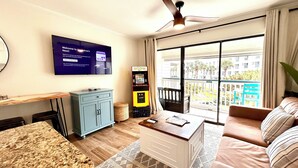 A modern living room with a flat-screen TV, a ceiling fan, a sofa, a coffee table, and a view of the outside balcony. - Updated 1-bedroom on Galveston’s seawall with ocean view, children’s bunks, wifi (Galveston)