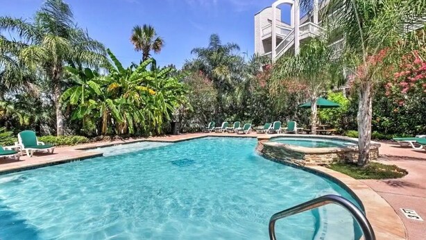 A swimming pool with clear blue water, surrounded by lounge chairs and palm trees. - Updated 1-bedroom on Galveston’s seawall with ocean view, children’s bunks, wifi (Galveston)
