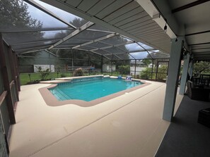 An indoor swimming pool with a covered roof, surrounded by a patio area with seating and a view of the backyard. - Central Florida Pool Home (DeBary)