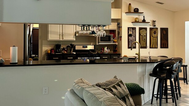 A modern kitchen with a central island, a dining area with bar stools, and a cozy seating area with a sofa. - Central Florida Pool Home (DeBary)