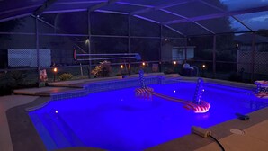 A covered outdoor swimming pool with a blue-lit water feature and a slide. - Central Florida Pool Home (DeBary)