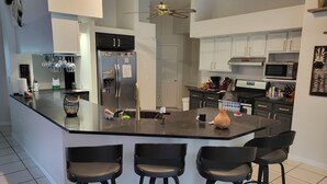A modern kitchen with a central island, bar stools, a refrigerator, microwave, and a ceiling fan. - Central Florida Pool Home (DeBary)