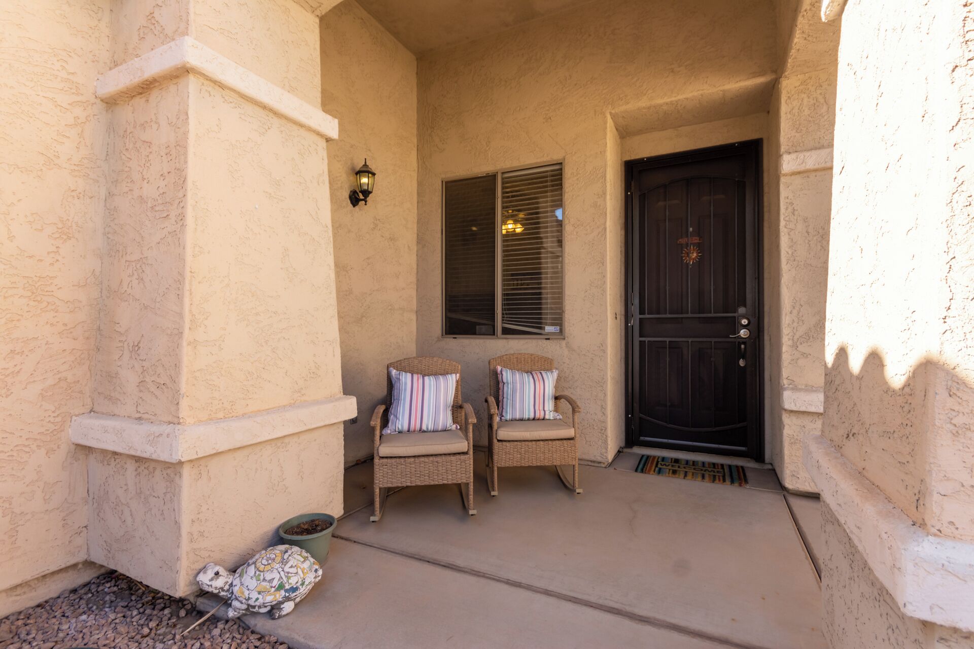 A covered porch with two wicker chairs and a mosaic turtle sculpture.