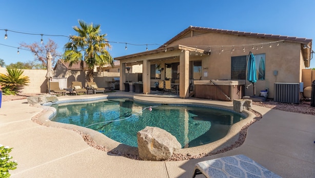 Un patio trasero con piscina, mobiliario de exterior y una zona de estar cubierta.