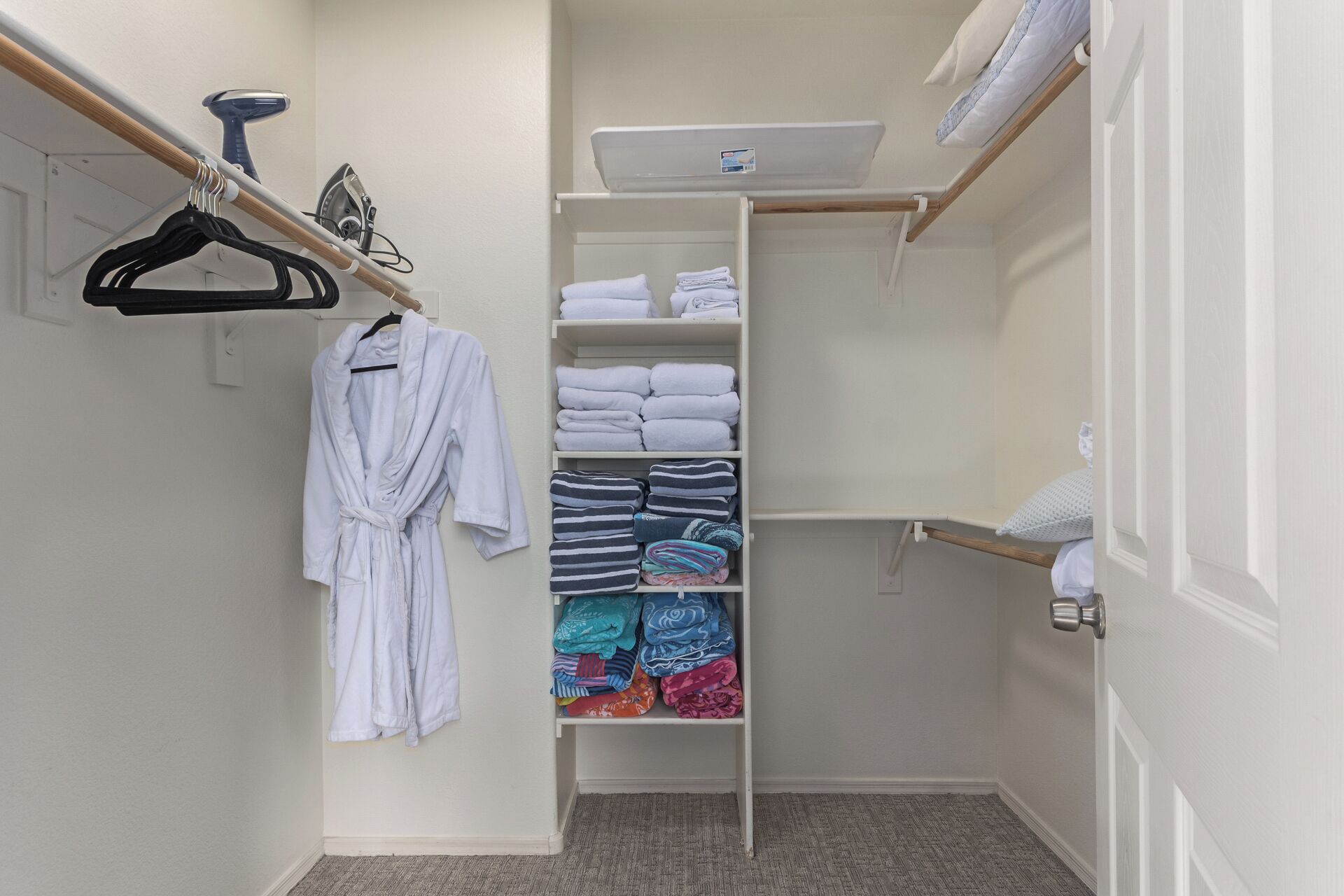 A walk-in closet with a hanging rack, shelves with folded towels, and a white robe hanging on the wall.