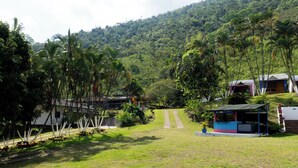 A rural setting with a grassy area, a few small buildings, and a hill in the background.