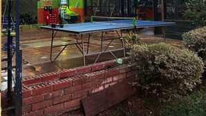 An outdoor area with a ping pong table, a brick wall, and a covered seating area with a wooden roof.