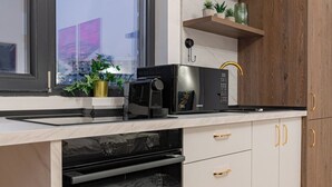 A modern kitchen with a built-in oven, a microwave, and a coffee maker on the countertop. There are wooden cabinets with gold handles and a window with a view of the outside. - Central Square Haven B (București)