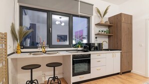 A modern kitchen with a large window, white cabinets, a black countertop, and two stools. - Central Square Haven B (București)