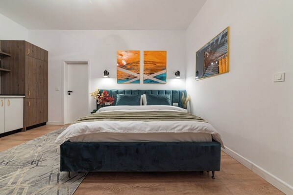Quarto moderno com cama, mesa de cabeceira, cômoda e obras de arte nas paredes.