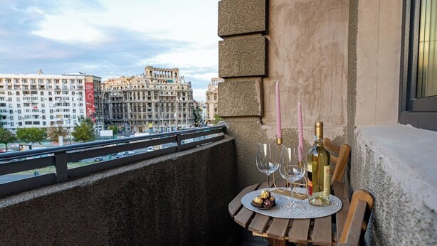 Een balkon met een tafel voor twee personen, compleet met een fles wijn, twee glaasjes en een bord chocolade.