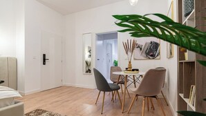 Een moderne woonkamer met een bank, een eettafel met stoelen en een salontafel. Er staat een boekenkast met boeken en decoratieve voorwerpen.