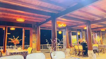 An outdoor restaurant with tables and chairs, wooden beams, and decorative lighting.