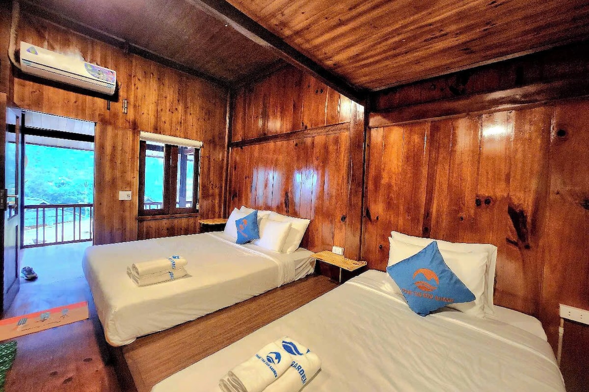 A wooden cabin room with two beds, a window, and an air conditioning unit.