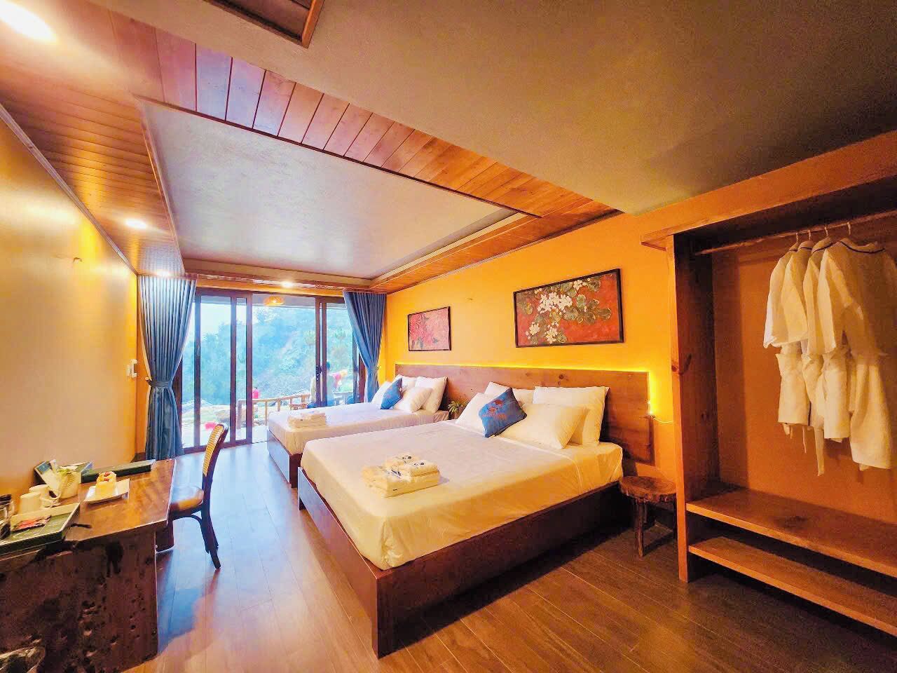 A room with two beds, a wooden desk, and a view of the outdoors.