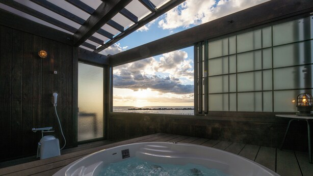 Ein Whirlpool auf einer Holzterrasse mit Blick auf den Sonnenuntergang über dem Meer.