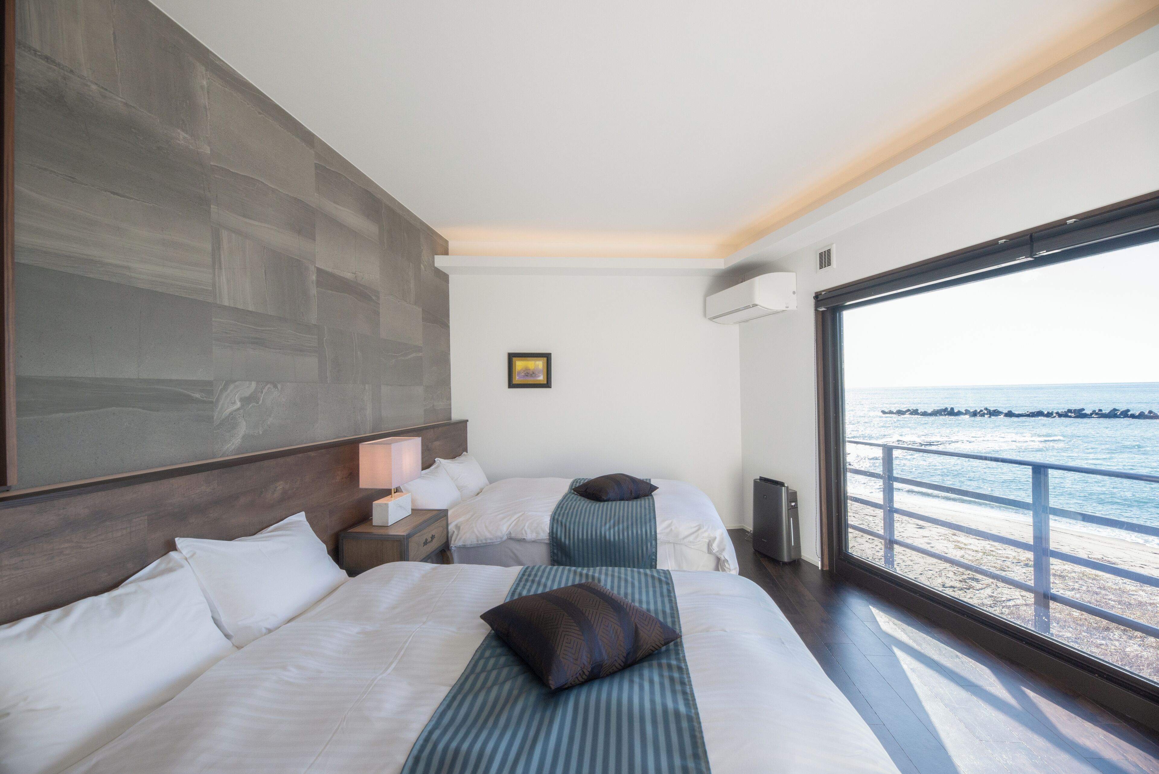 Une chambre d’hôtel avec deux lits, une grande fenêtre donnant sur la mer et un design moderne.